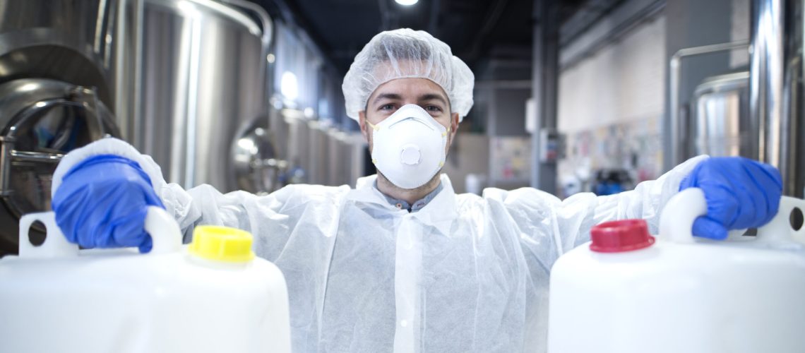 Industrial worker with protective mask and white uniform holding plastic cans for chemical industry.